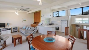 A modern living room with a dining table, kitchen, and large windows. - Paradise Court 6, Tura Beach (Tura Beach)