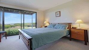 Une chambre avec un lit, deux tables de chevet avec des lampes, une chaise et une porte-fenêtre coulissante donnant sur un balcon avec vue.