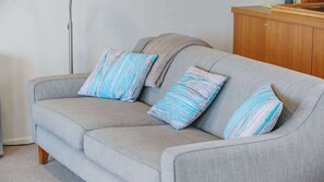 Un canapé gris avec des coussins à rayures et, au fond, un meuble en bois.