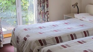 A room with two beds, a window with curtains, a bedside table, and a lamp. - Town House, situated in the village Salthill close to the seafront. (Galway)