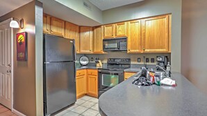 A kitchen with wooden cabinets, a stainless steel refrigerator, a microwave, an oven, and a granite countertop. - 10 Mi to Beach: Legends Resort Condo on Ninth Hole (Myrtle Beach)
