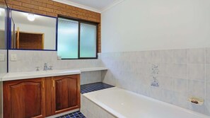 Ein Badezimmer mit Badewanne, Holzschränken, einem Spiegel und einem Fenster mit Milchglas.