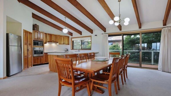 A spacious kitchen with wooden cabinets, a dining table with chairs, and a large window with a view of greenery.
