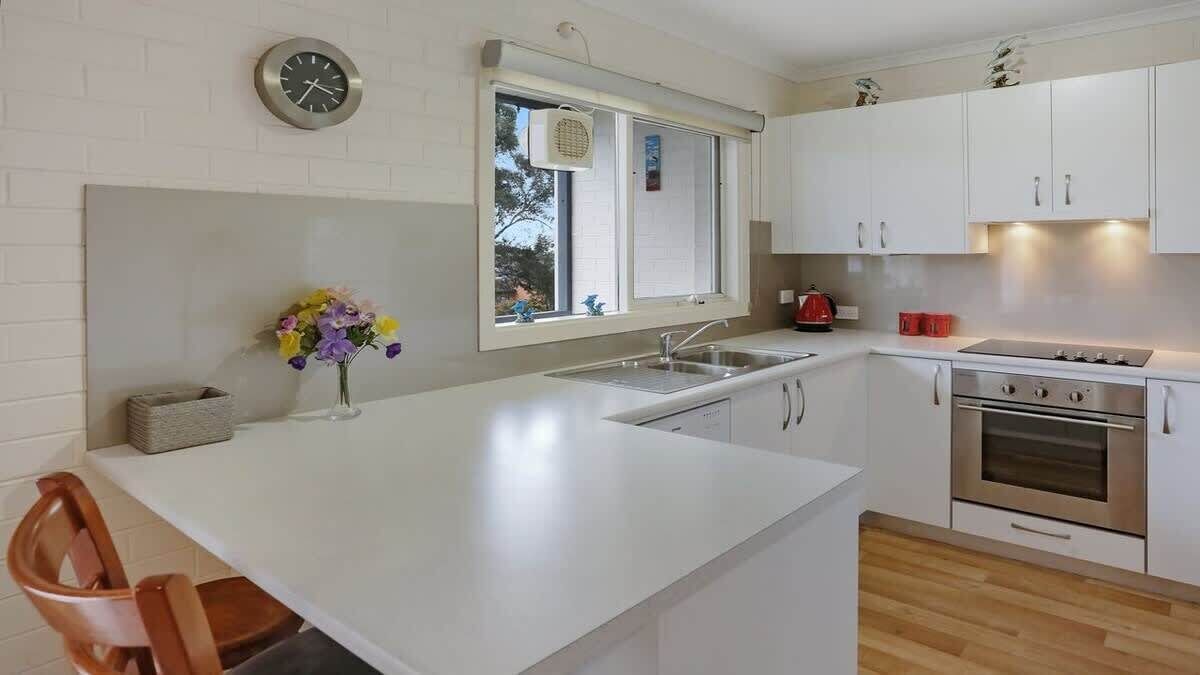 A kitchen with white cabinets, a stainless steel oven, a sink, and a window with blinds.