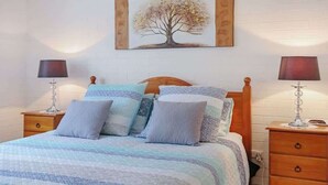A bed with a wooden headboard, two bedside tables, and a wall-mounted lamp. - North Terrace 9 (Merimbula)
