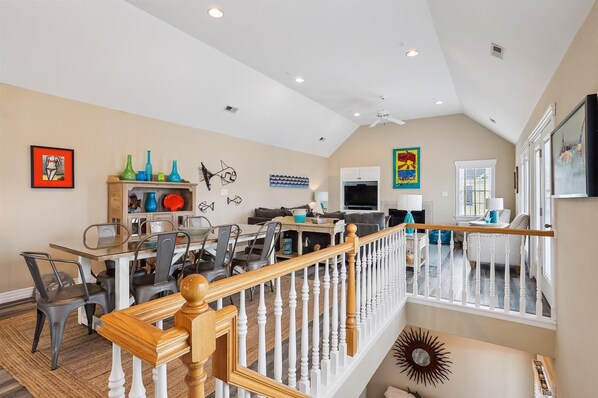 A spacious living area with a dining table, chairs, a kitchen area, and a staircase with a wooden railing.