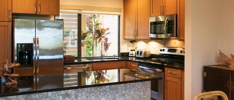 Una cocina con armarios de madera, electrodomésticos de acero inoxidable, una isla grande con taburetes y un protector contra salpicaduras de piedra.