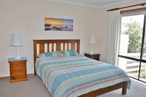 A bedroom with a bed, two bedside tables with lamps, a window with curtains, and a painting on the wall.