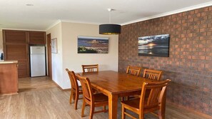 A dining area with a wooden table and chairs, a brick wall, and two framed pictures.