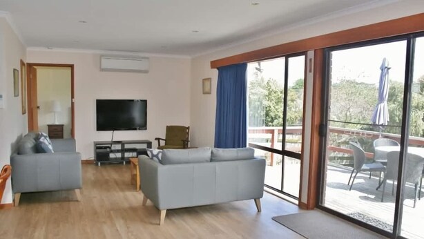 Een woonkamer met een bank, een televisie en een balkon met buitenmeubilair.