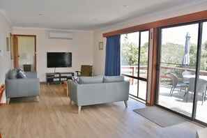 A living room with a sofa, a television, and a balcony with outdoor furniture. - Laura's at Pambula Beach (Pambula Beach)