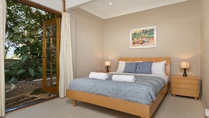 Quarto com uma cama grande, duas mesas de cabeceira, um quadro na parede e uma porta de vidro deslizante para um jardim.