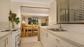 Uma cozinha moderna com armários brancos, uma área de jantar com mesa e cadeiras de madeira, e uma grande janela com persianas.