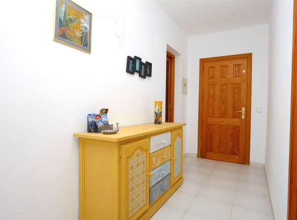 A hallway with a wooden door, a yellow console table with a decorative item, and a framed picture on the wall.