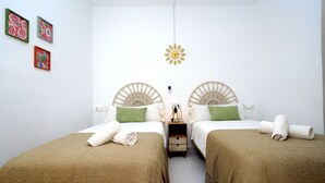 Habitación doble con dos camas, cada una con cabecera, mesita de noche pequeña y lámpara de pared. Hay tres cuadros enmarcados en la pared.