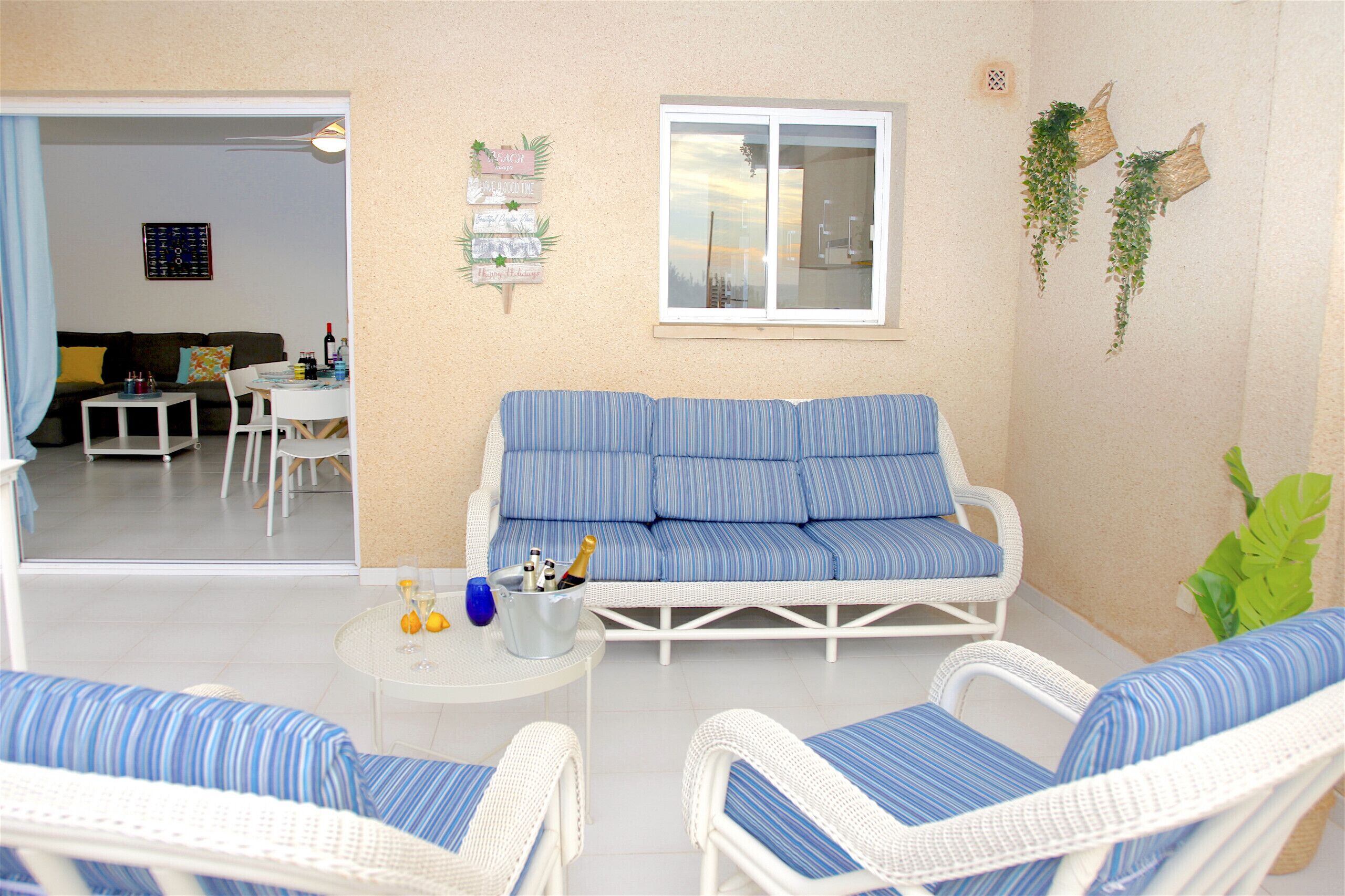 A living room with a sofa, two armchairs, a small table with a drink and bottle, and a window.