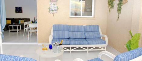 A living room with a sofa, two armchairs, a small table with a drink and bottle, and a window.