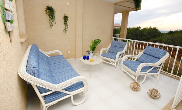 A balcony with two wicker lounge chairs, a small round table with a drink and a plant, and a white railing.
