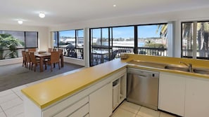 A modern kitchen with large windows, a dining area, and a view of the outdoors. - The Escape (Merimbula)