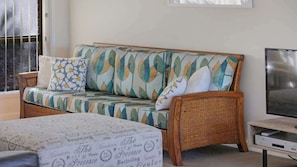 Une pièce comprenant un canapé en osier, un téléviseur et un lit recouvert d’une couvre-lit à motifs.