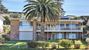 A two-story residential building with a balcony, a garage, and a palm tree in the front yard. - The Escape (Merimbula)