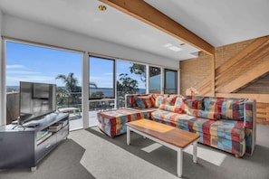 A modern living room with a sofa set, a coffee table, a TV, and a staircase. - Seaview Pambula Beach (Pambula Beach)