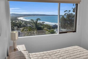 A bedroom with a large window overlooking a beach and ocean.