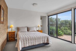 A bedroom with a large bed, two bedside tables with lamps, a sliding glass door to a balcony, and a brick wall. - Seaview Pambula Beach (Pambula Beach)