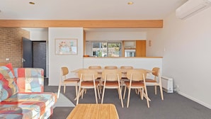 A modern living room with a sofa, a dining table with chairs, a coffee table, and a kitchen area with a window. - Seaview Pambula Beach (Pambula Beach)