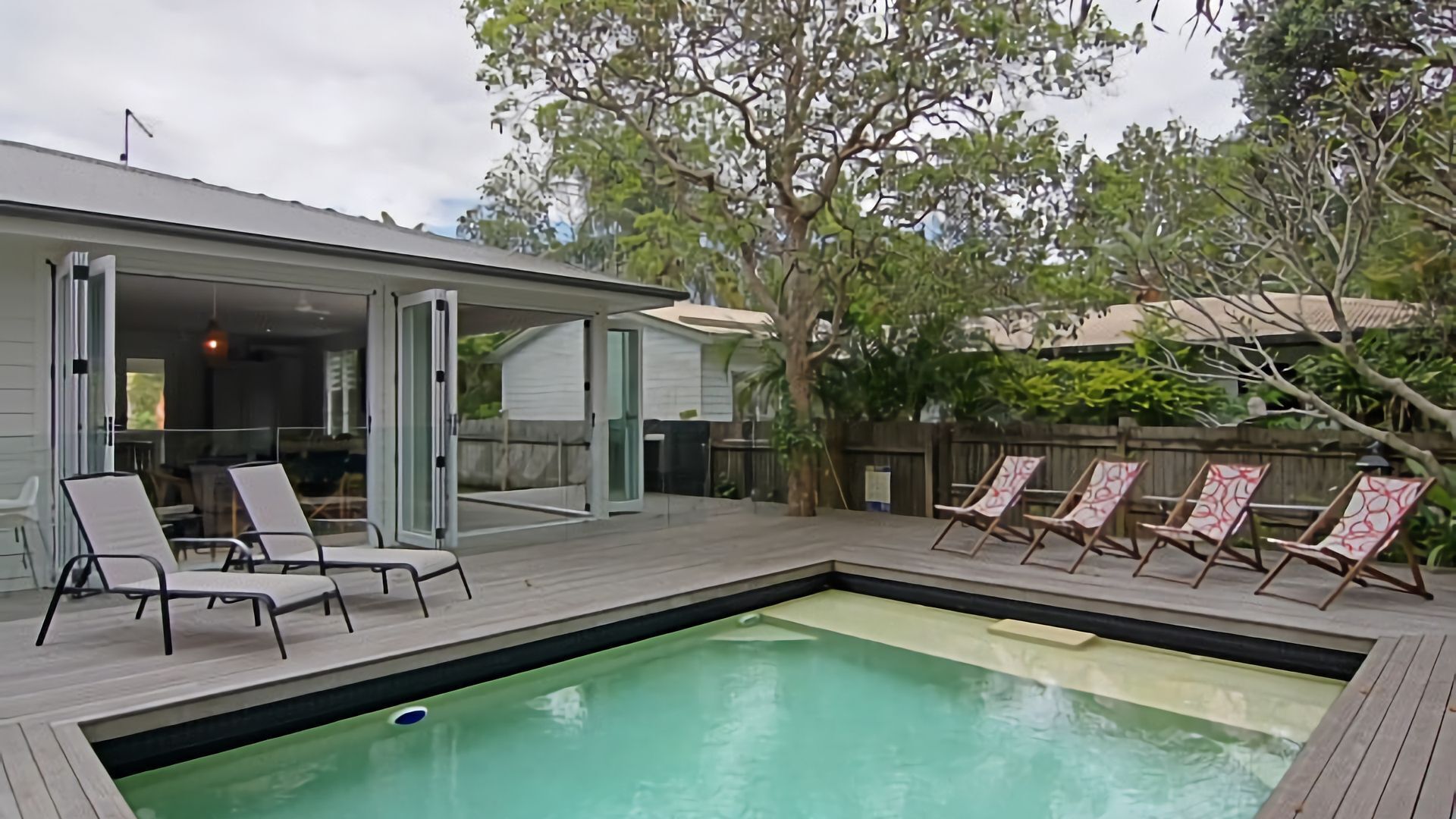 A backyard with a swimming pool, lounge chairs, and a covered patio area.