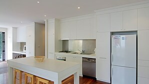 Une cuisine moderne avec des meubles blancs, un îlot central, des appareils en acier inoxydable et une table à manger en bois.