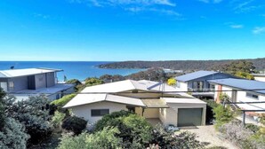 A coastal residential area with houses, a clear sky, and a view of the sea. - Sullivan's on Kanangra (Pambula Beach)