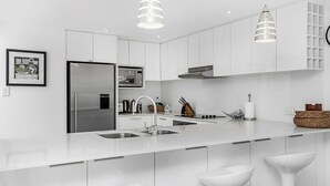 A modern kitchen with white cabinetry, stainless steel appliances, a double sink, and pendant lighting. - Byron Bay Accom - Eastpoint 2 - 18 - 20 Paterson Lane (Byron Shire)