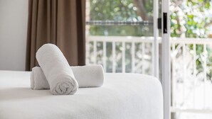 A neatly made bed with white linens and a rolled towel on top, a window with curtains, and a balcony with a railing. - Byron Bay Accom - Eastpoint 2 - 18 - 20 Paterson Lane (Byron Shire)