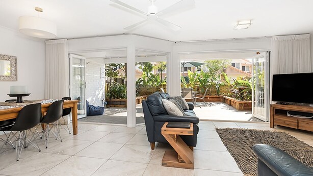 A spacious living area with a modern sofa, a dining table with chairs, a flat-screen TV, and a balcony with plants. - Byron Bay Accom - Eastpoint 2 - 18 - 20 Paterson Lane (Byron Shire)