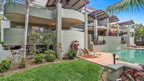 Un edificio moderno de varios pisos con piscina, zona de estar al aire libre y jardines exuberantes.