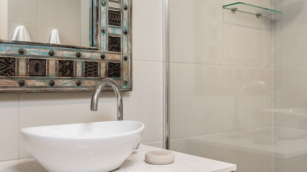 A bathroom with a white sink, a mirror with a distressed frame, and a shower area.