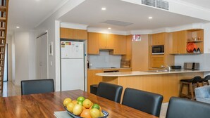 Una cuina moderna amb armaris de fusta, un forn de microones integrat i una zona de menjador amb taula i cadires de fusta.