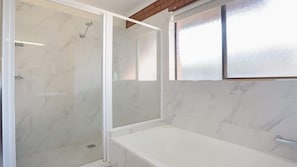 Une salle de bain équipée d’une douche, d’une baignoire et d’une fenêtre en verre dépoli.