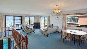 Ein großzügiges Wohnzimmer mit einer Couch, Sesseln, einem Fernseher und einem Balkon mit Blick.