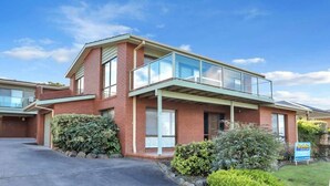 A two-story brick building with a glass balcony, a driveway, and a signboard.