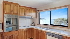 A kitchen with wooden cabinets, stainless steel appliances, a large window with a view of the sea, and a dishwasher.