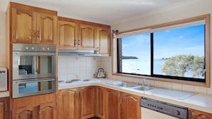 Eine Küche mit Holzausstattung, Edelstahlgeräten, einem großen Fenster mit Meerblick und einem Geschirrspüler.