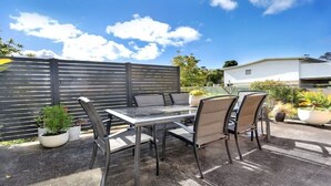 An outdoor patio with a table and chairs, surrounded by potted plants and a fence. - PiPis on Collins (Merimbula)