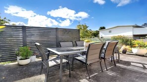 An outdoor patio with a table and chairs, surrounded by potted plants and a fence.