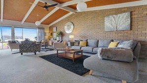 A modern living room with a brick wall, a ceiling fan, a large window, and a sofa with cushions. - PiPis on Collins (Merimbula)