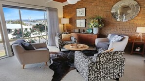 A modern living room with a large window, a brick wall, and a round mirror. - PiPis on Collins (Merimbula)