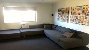A living room with a sectional sofa, a large window with blinds, and a wall decorated with a collage of images.