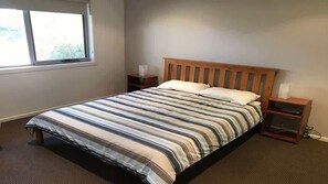 A bedroom with a bed, a window, a nightstand, and a bedside table. - Turaroo (Tura Beach)