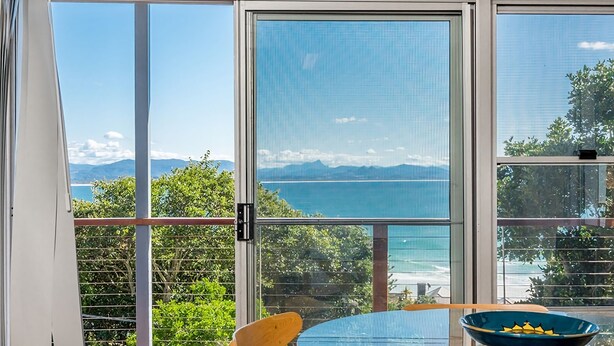 A room with a large window offering a view of the sea and mountains.